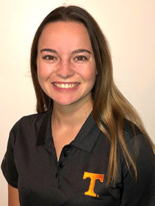 A smiling young woman with long, straight blonde hair wearing a dark gray polo shirt with a UT Power T insignia