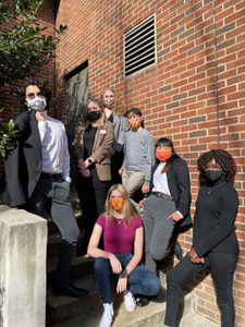 Seven council members, wearing cloth face coverings, strike curious yet hip poses outside a residence hall