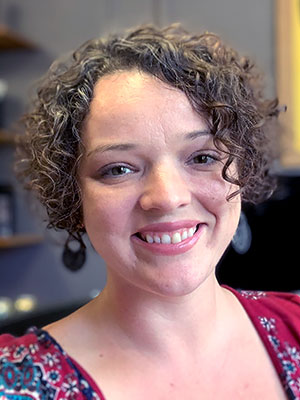 A smiling woman with short curly hair and large earrings, wearing a red patterned top