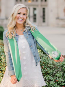 A smiling young woman with long blonde hair wearing a white dress, jean jacket, and green honors stole 